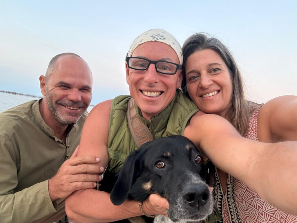 Patrick Gaveau avec ses amies Tina et Bela, souriantes, posant avec un chien, illustrant l’importance de l’amitié et de la communauté pour le bien-être.
