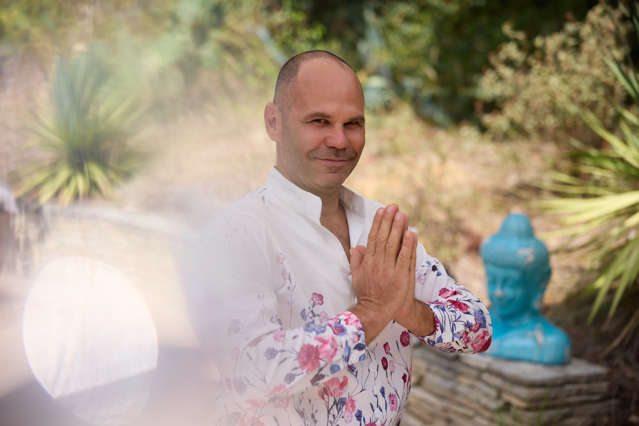 Patrick Gaveau en position de Namaste, souriant, portant une chemise à fleurs au cœur de la nature, incarnant sérénité et présence.