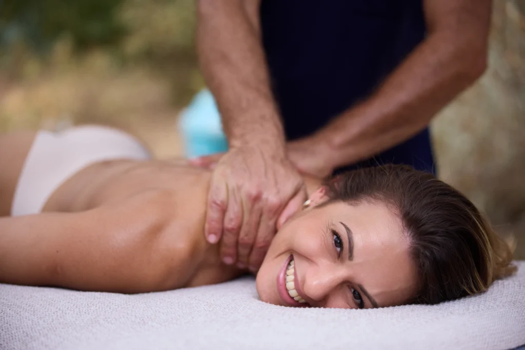 Femme allongée sur une table de massage, souriante, recevant un massage relaxant du cou pour libérer les tensions et favoriser le bien-être.