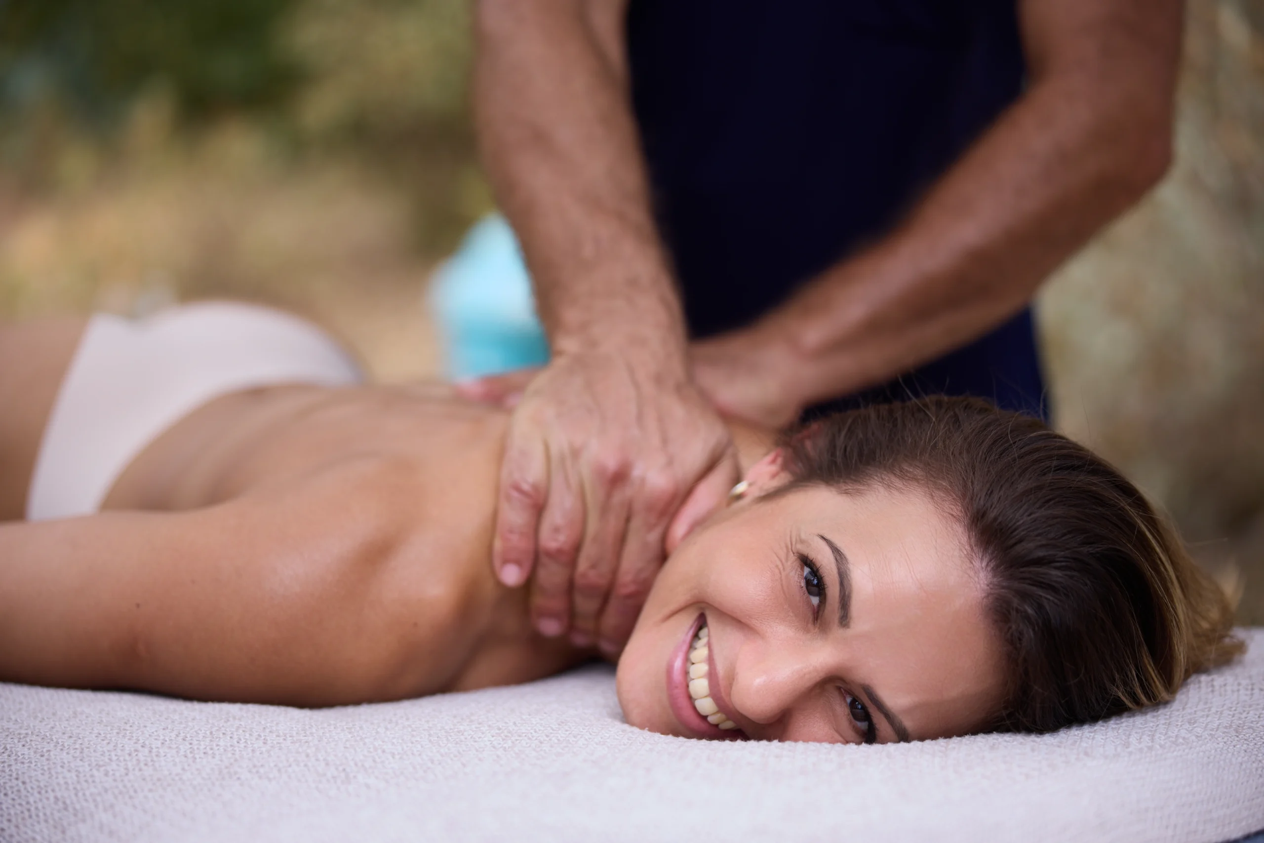 Femme allongée sur une table de massage, souriante, recevant un massage relaxant du cou pour libérer les tensions et favoriser le bien-être.